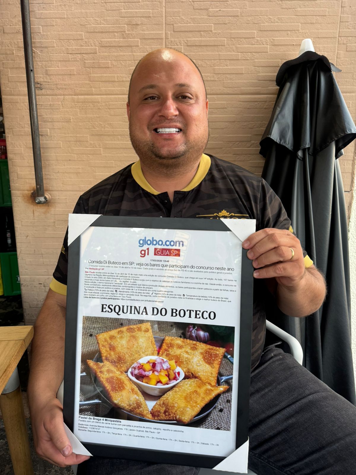 Maycon, dono do Esquina do Boteco, segurando materia do G1 Globo sobre participacao no concurso Comida di Buteco 2026 em Sao Paulo